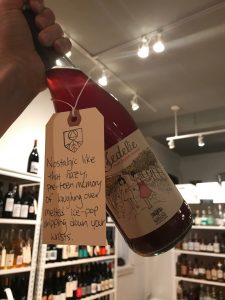 interior of a well-lit wine shop with an image of a pink bubbly wine. There is a branded tag on it that says "Nostalgic like that hazy, pre-teen memory of laughing over melted ice-pop dripping down your wrists."