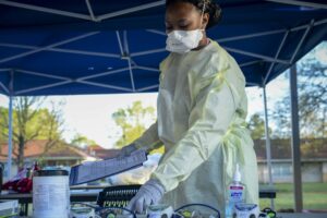 A person in protective medical gear handles testing equipment