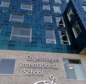 Copenhagen International School- shows the front of the building with transparent windows and tinted tiles in various shades of blue.