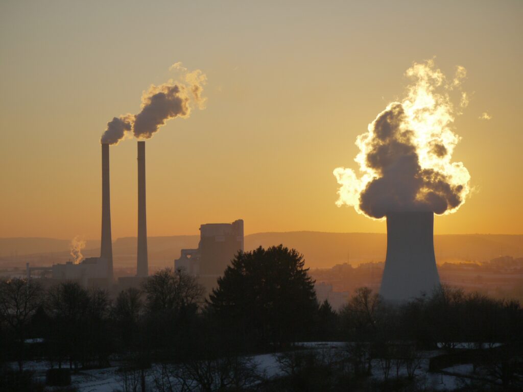 Silhouettes of fossil fuel smokestacks in a yellow sunset